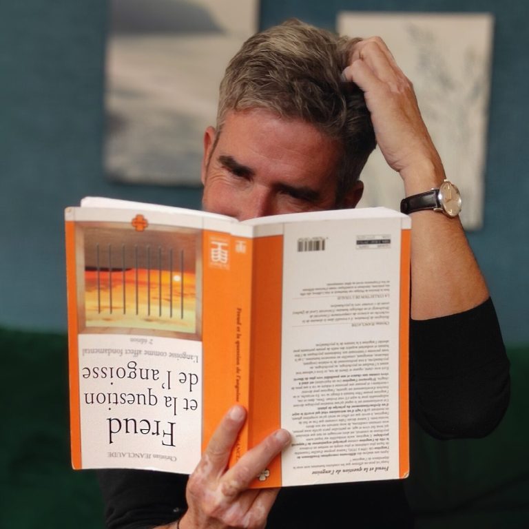 Alain KREMER - psychanalyste à Lyon feuilletant un livre sur Freud, l'air perplexe, dans un cadre intérieur.