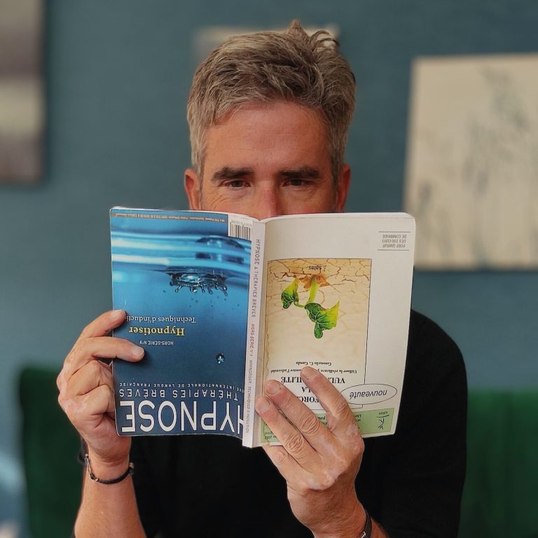 Alain KREMER -Hypnothérapeute à Lyon  lisant un livre sur l'hypnose, cachant son visage derrière la couverture.