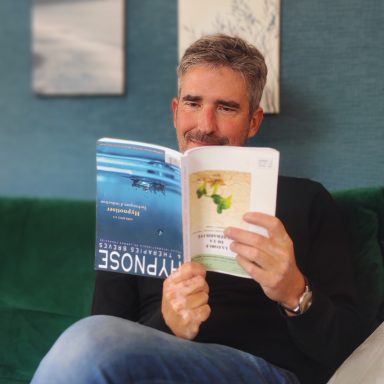 Homme souriant lisant un livre sur un canapé vert.